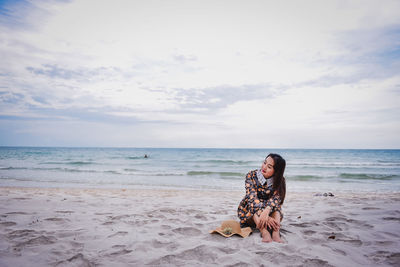 Woman sitting on beach by sea against sky