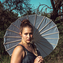 Portrait of woman holding umbrella while standing against trees