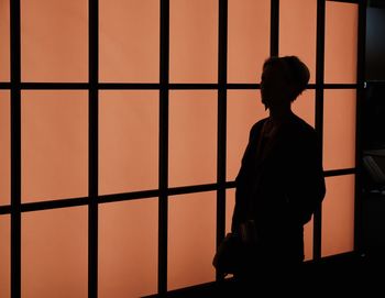 Silhouette of woman standing against illuminated window