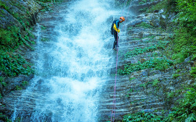 Full length of man climbing rock by waterfall