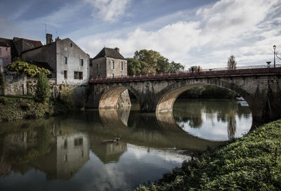 Bridge over river by buildings against sky