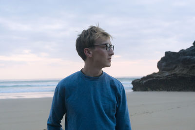 Close-up of young man looking away standing at beach against sky