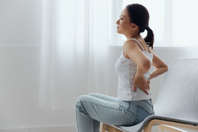Young woman with back pain sitting on chair