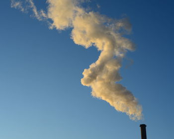 Low angle view of smoke emitting from chimney against blue sky