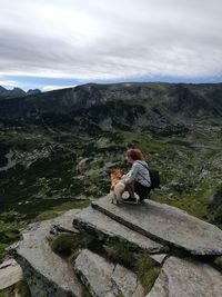 Dog sitting on rock by mountain against sky