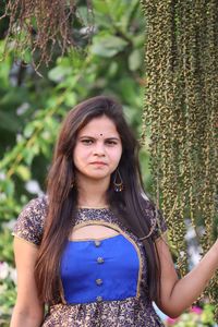 Portrait of beautiful young woman standing by tree trunk