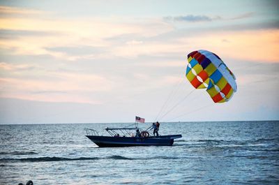 People with parachute in boat on sea against sky during sunset