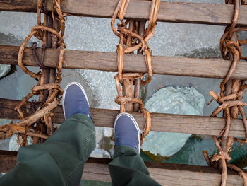 Low section of man standing on rope bridge over sea