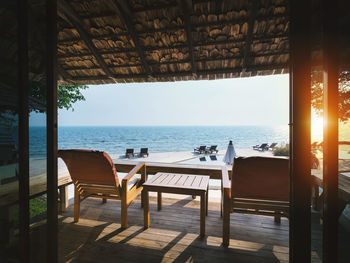 Chairs and table at restaurant by sea against sky