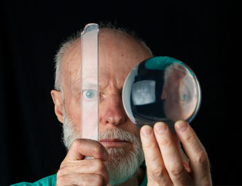 Close-up portrait of man holding camera over black background