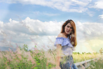 Portrait of smiling young woman standing against sky