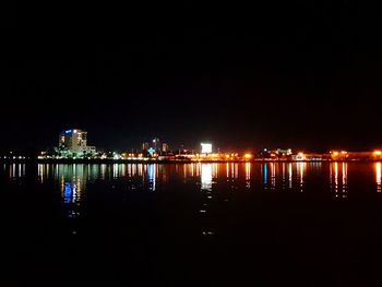 Illuminated city by river against sky at night