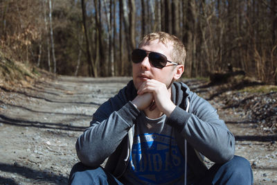 Man wearing sunglasses while sitting on dirt road in forest