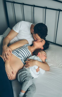 Close-up of man and woman kissing by baby on bed at home