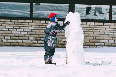 Boy playing with snow in yard during winter