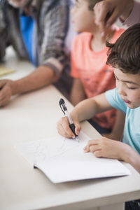 High angle view of boy drawing in book at table by family