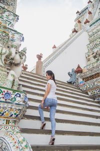 An asian woman in a white t-shirt looking at a camera at the wat arun temple while traveling