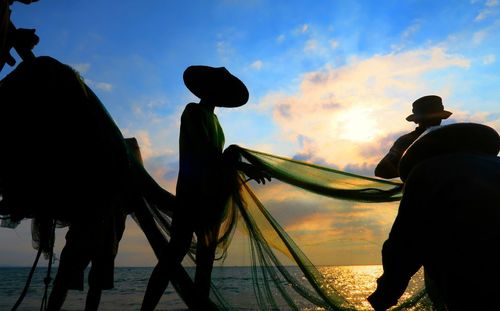Low angle view of fishermen holding net at beach against sky during sunset