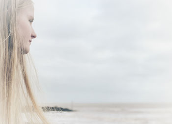 Portrait of young woman looking at sea against sky