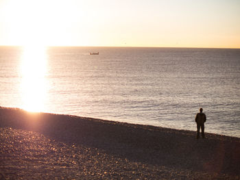Silhouette man standing on beach against clear sky during sunset