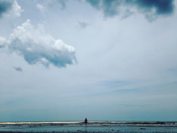 Rear view of man standing in sea against cloudy sky