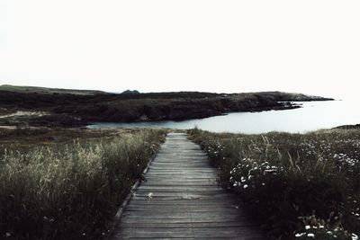 Boardwalk leading towards landscape against clear sky