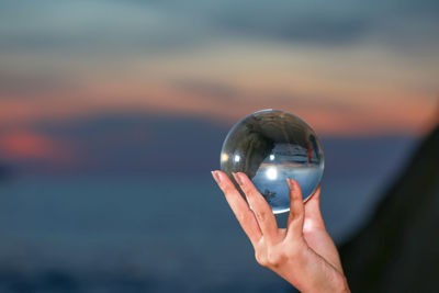 Close-up of hand holding crystal ball against blurred background