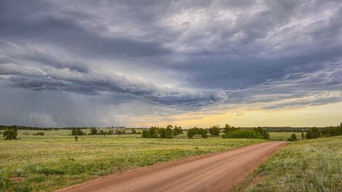 Dirt road amidst field against sky