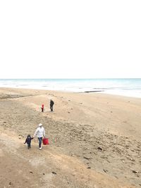 Rear view of men walking on beach against clear sky