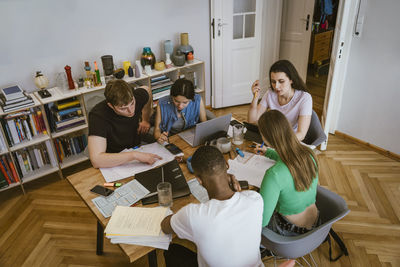 High angle view of friends studying while doing homework at dining table