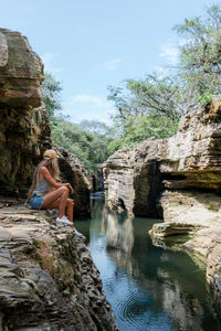 Rear view of woman sitting on rock by lake