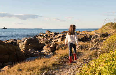 Rear view of woman standing on rock by sea against sky