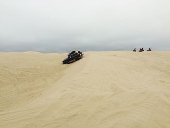 Off-road vehicle on sand dune in desert against sky