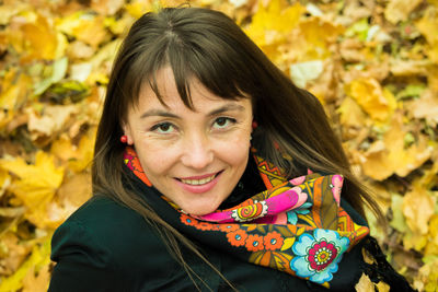 Portrait of smiling mid adult woman sitting on autumn leaves at park