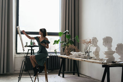 Side view of woman painting on canvas at art studio