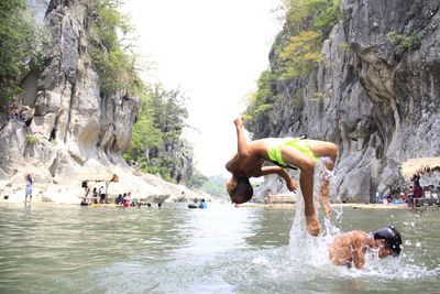 Boy jumping in river against rocky mountains