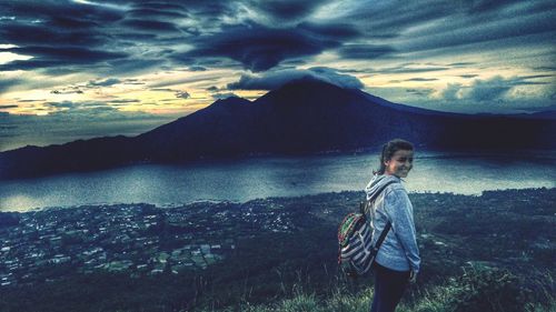 Young woman standing by lake against sky during sunset