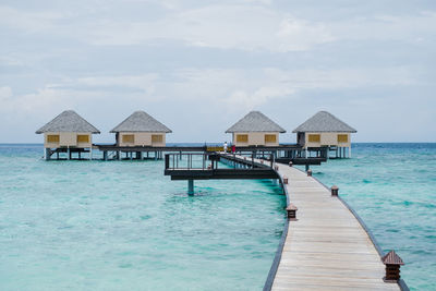 Stilt houses on pier by sea against sky