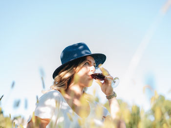 Low angle view of young woman drinking wine against sky