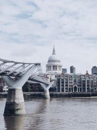 Bridge over river in city against cloudy sky