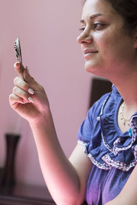 Mid adult woman looking in mirror while sitting against wall at home