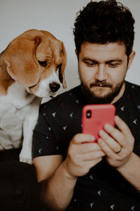 Portrait of man holding dog while using smart phone