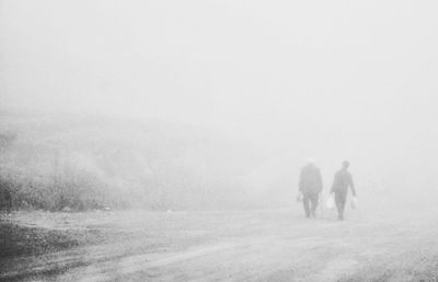 Rear view of men walking on snow covered field during foggy weather