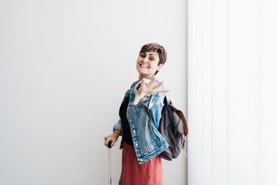 Portrait of smiling young woman standing against wall