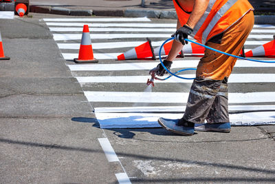 A road worker applies white road markings to a crosswalk using an airbrush and a wooden template 