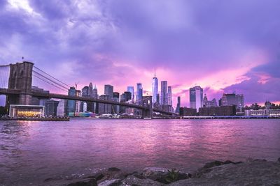 Bridge over river by buildings against sky at dusk