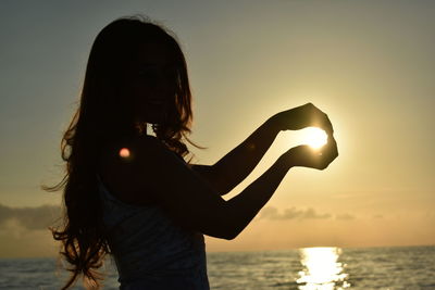 Optical illusion of woman holding sun at beach during sunset