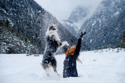 Cheerful woman playing with dog on snow covered field