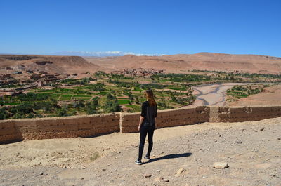 Rear view of woman standing on landscape against clear blue sky