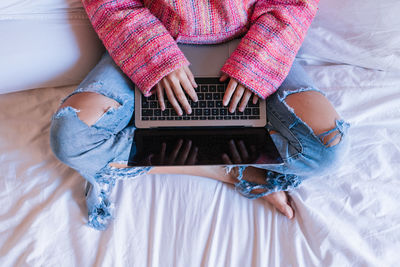 Low section of woman using laptop while sitting on bed at home